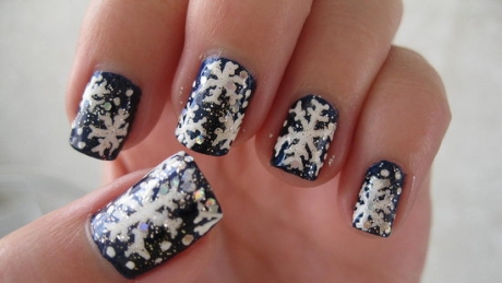 Close-up of nails painted navy blue with white snowflake designs on every finger.